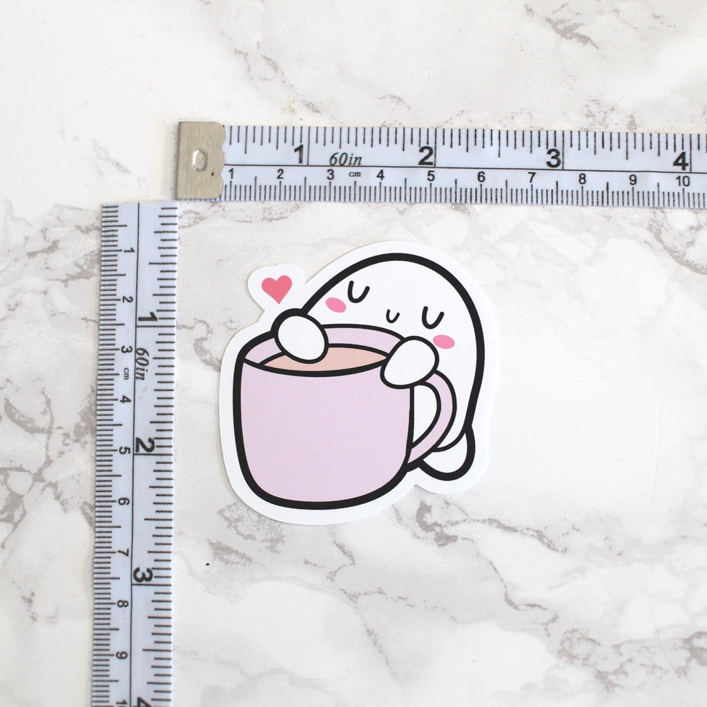 Cartoon ghost holding a cup with a heart on a marble surface with a ruler for scale.