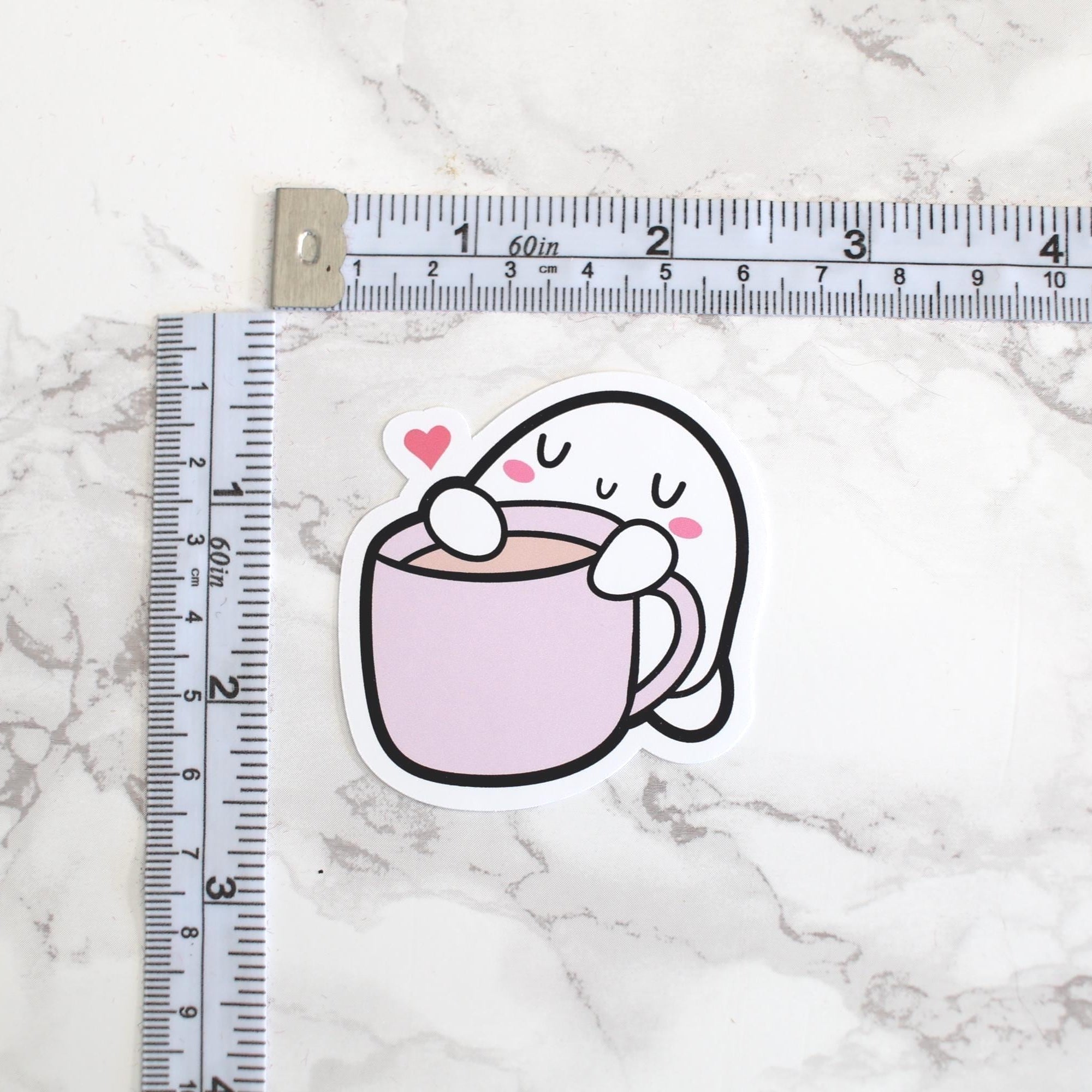 Cartoon ghost holding a cup with a heart on a marble surface with a ruler for scale.