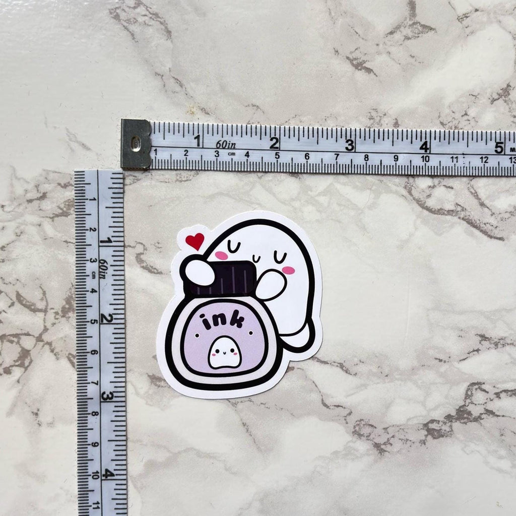 Sticker of a camera with a heart on a marble surface next to a ruler.
