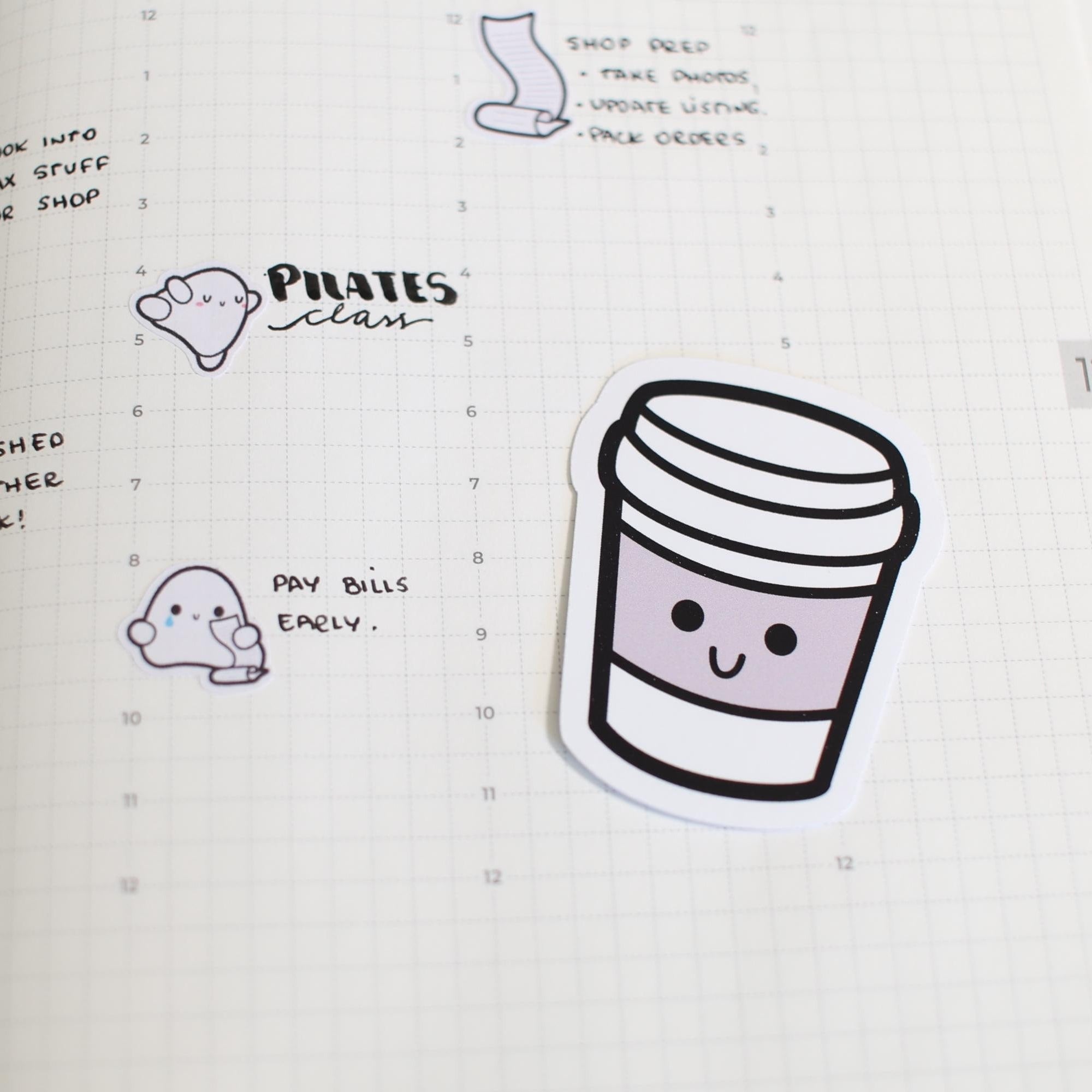 Planner stickers on grid paper depicting a daily planner page with a smiling purple coffee cup sticker, a happy white blob character sticker for "Pilates class," and a sad white blob character sticker holding a scroll for "Pay bills early"