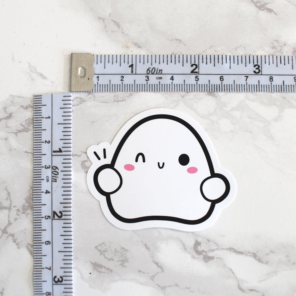 Cartoon ghost sticker next to a ruler on a marble surface