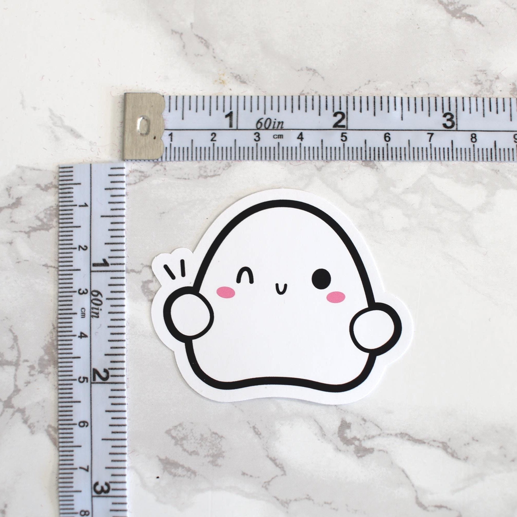 Cartoon ghost sticker next to a ruler on a marble surface