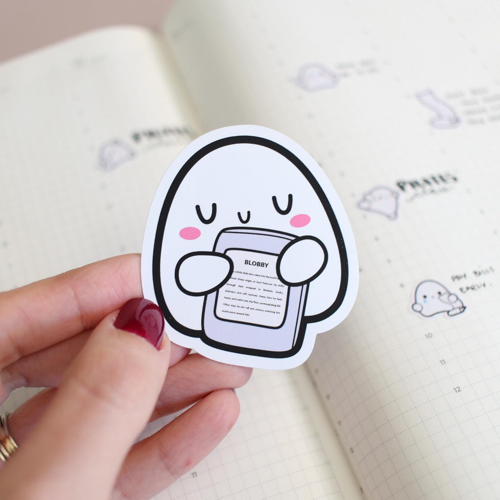 Sticker of a cartoon ghost holding a phone with a hand holding it, on a notebook background.