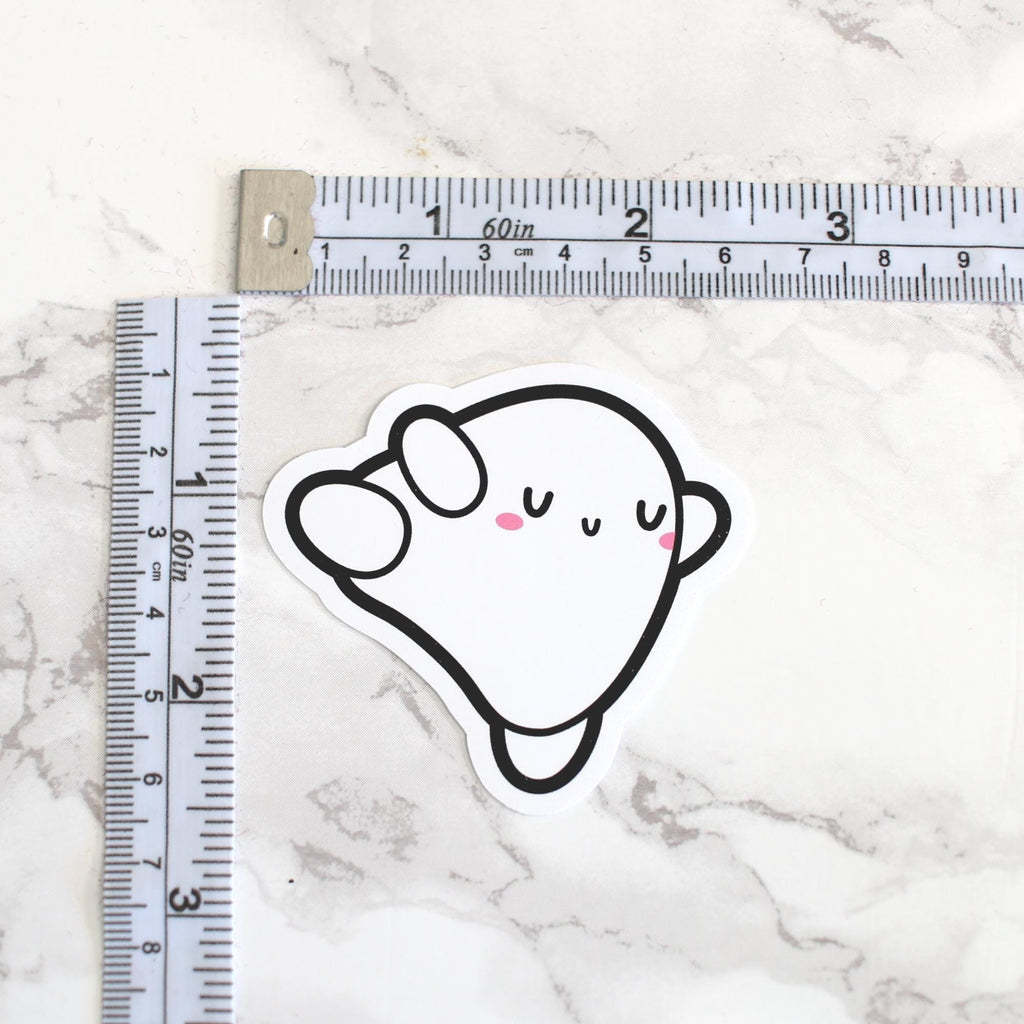 Sticker of a cartoon ghost with a ruler for scale on a marble surface