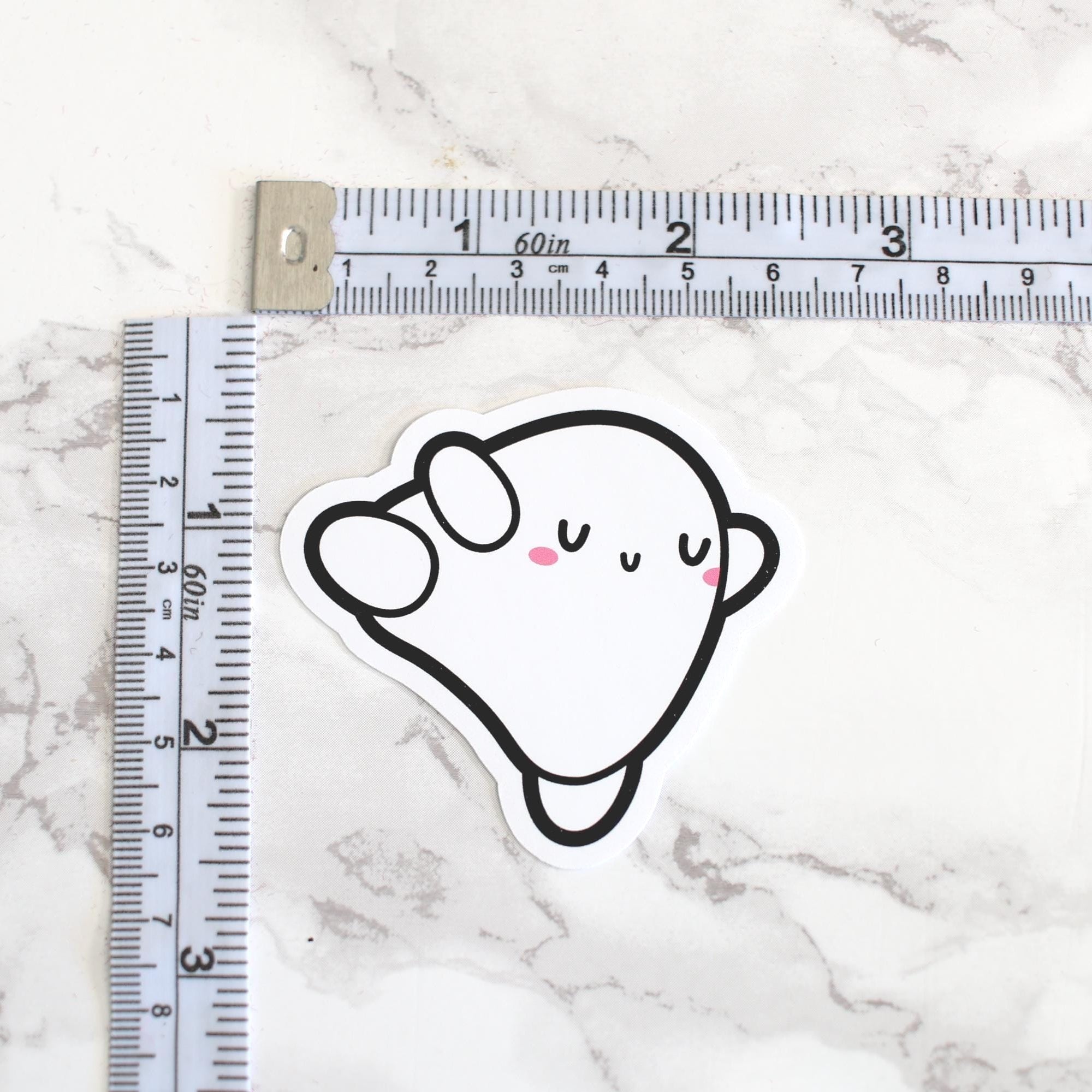 Sticker of a cartoon ghost with a ruler for scale on a marble surface