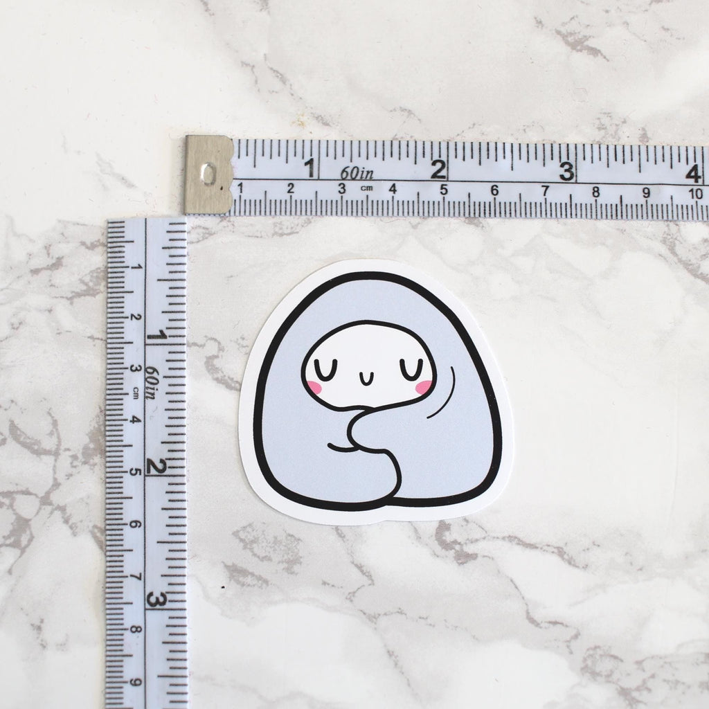 Sticker of a cartoon ghost with a smile on a marble surface with a ruler for scale.
