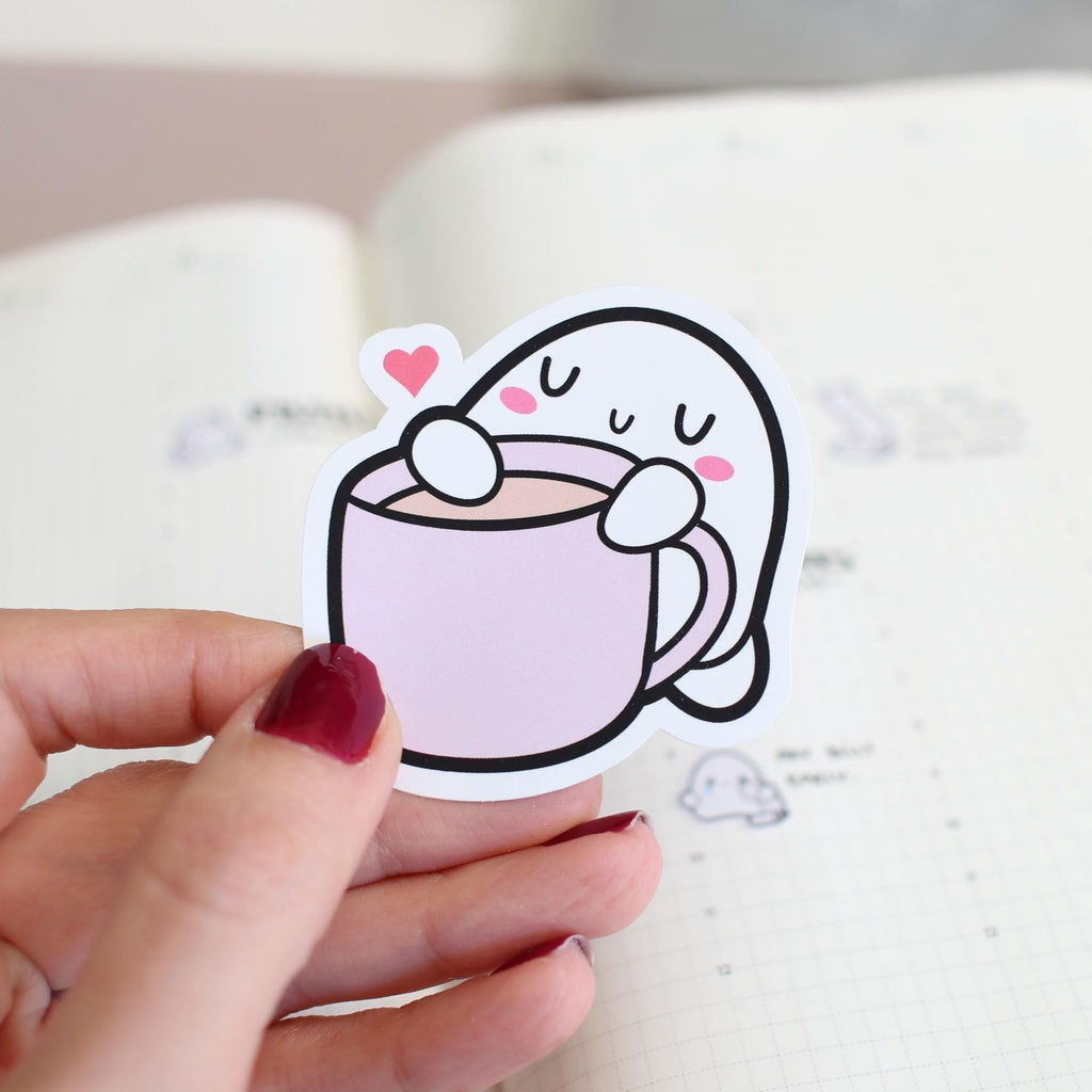 Cartoon sticker of a cup with a face held by a hand on a notebook background