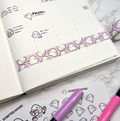A white gridded planner on a marble surface, featuring a strip of purple washi tape with smiling white ghost patterns, alongside hand-drawn ghost characters illustrating daily tasks like Pilates class and finished another book, with Scripted Hours ghost sticker sheets and pink and purple markers nearby