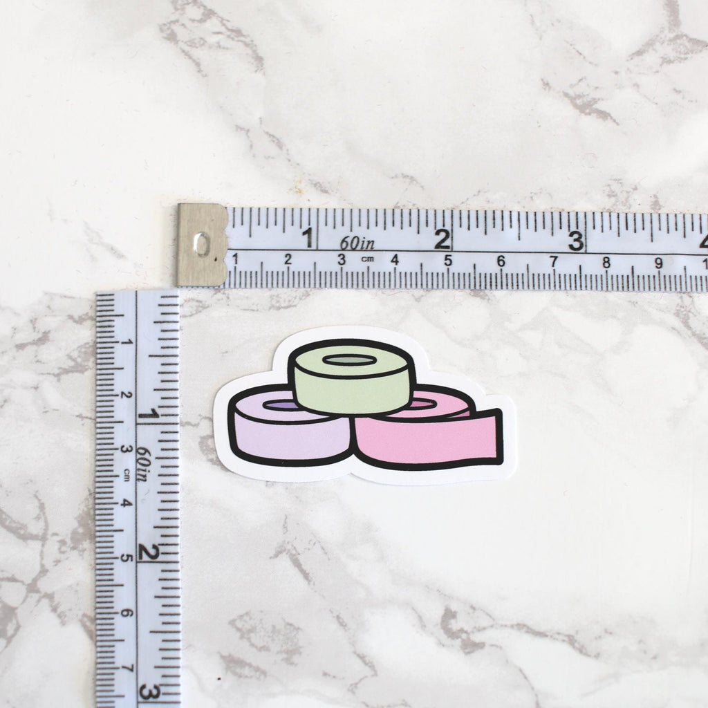 Three colorful washi tape rolls next to a ruler on a marble surface